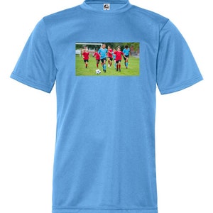 May include: A light blue t-shirt with a graphic of children playing soccer on a green field