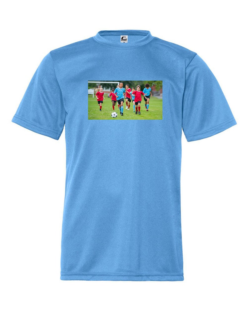 May include: A light blue t-shirt with a graphic of children playing soccer on a green field
