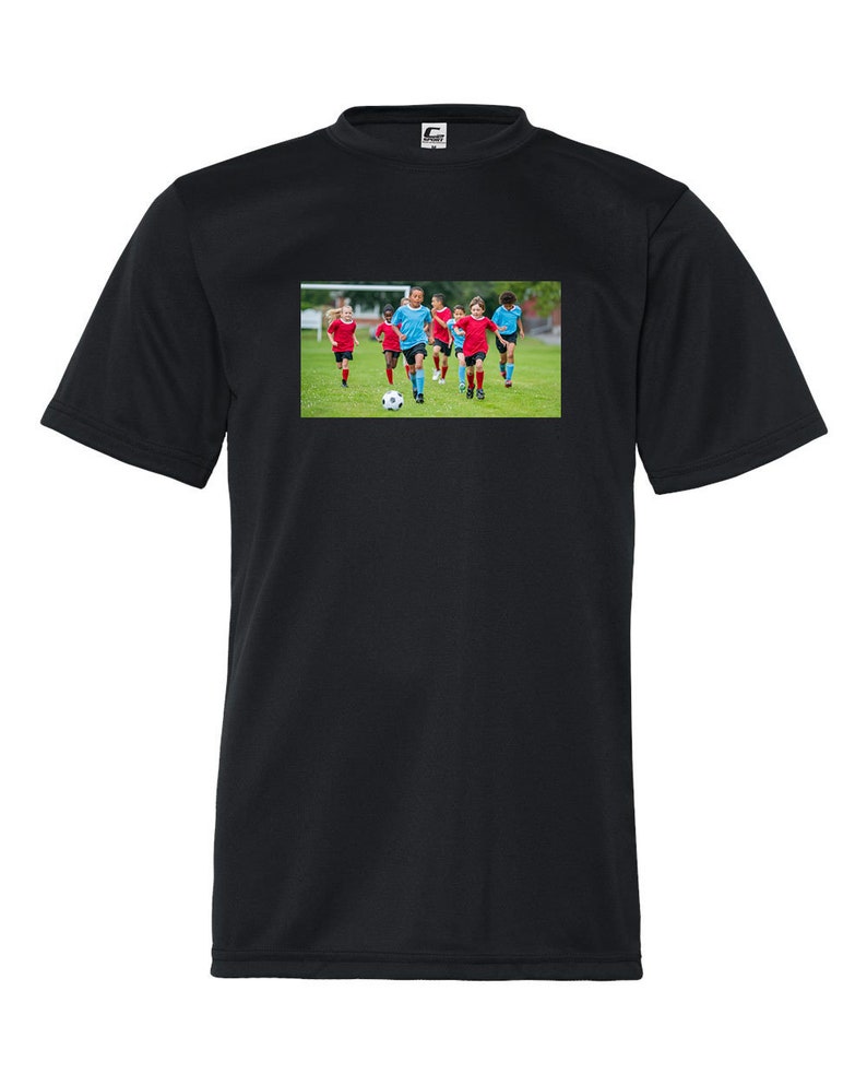 May include: A black t-shirt with a graphic of a group of children playing soccer on a green field. The children are wearing red and blue uniforms. The graphic is centered on the t-shirt.