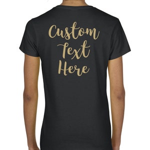 May include: A black short-sleeved t-shirt featuring the words Custom text Here printed in a gold-colored cursive script on the back. The shirt has a crew neckline and a standard fit, providing a plain black canvas for the gold lettering.