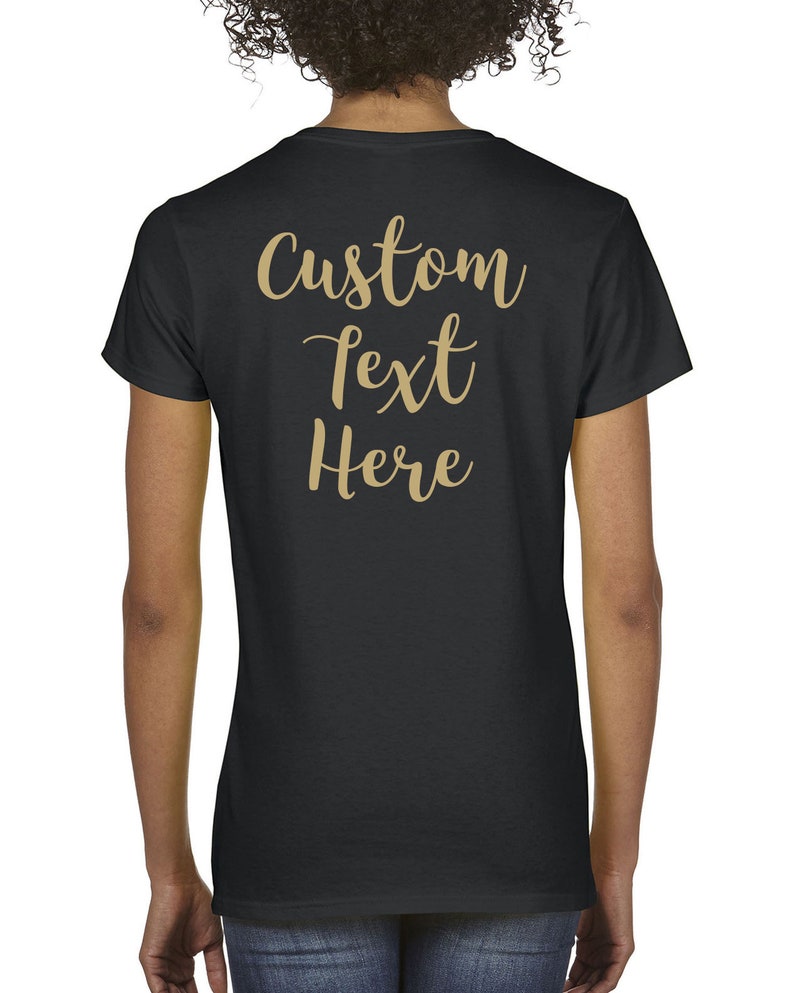 May include: A black short-sleeved t-shirt featuring the words Custom text Here printed in a gold-colored cursive script on the back. The shirt has a crew neckline and a standard fit, providing a plain black canvas for the gold lettering.