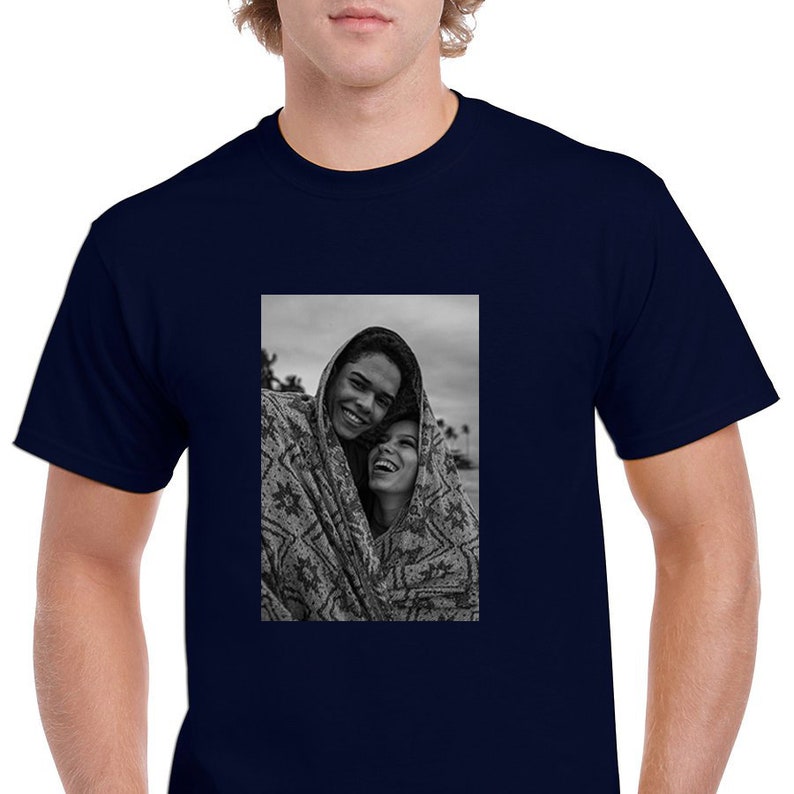 May include: Navy blue t-shirt featuring a black and white photograph of two people smiling and wrapped in a patterned blanket. The photograph is centered on the shirt.