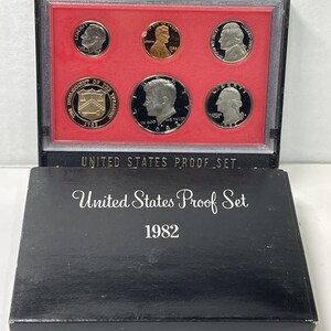 May include: A 1982 United States Proof Set in a black box. The set includes six coins displayed in a red-lined case. The box and case are labeled with the text "United States Proof Set". The coins feature various portraits and inscriptions.