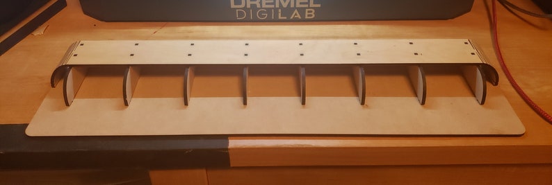 May include: A wooden shelf with seven compartments, each with a rounded opening. The shelf is made of light brown wood and has a natural finish.
