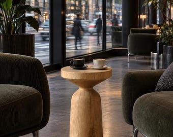 May include: A light-colored wooden side table with a cylindrical base and a wider circular top. Two ceramic coffee cups, one black and one white, each resting on a matching saucer, are placed on the surface of the wooden table.