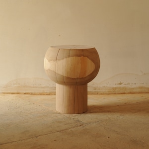 May include: A wooden stool with a round, bulbous top and a cylindrical base. The stool is made of light-colored wood with a natural finish.