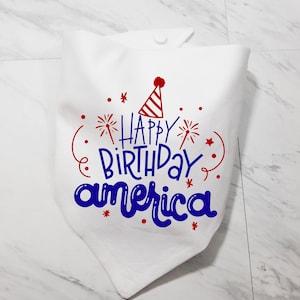 May include: White fabric bandana with red and blue text that says "Happy Birthday America" with a red and white party hat and red fireworks.