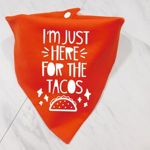 Op de afbeelding: Oranje bandana met witte tekst die "Ik ben hier alleen voor de taco's" zegt en een witte omtrek van een taco.