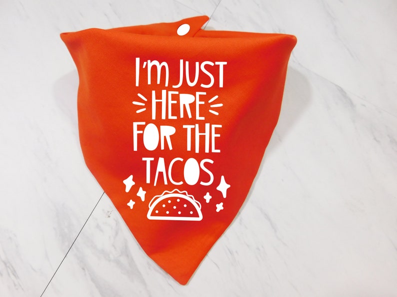 Op de afbeelding: Oranje bandana met witte tekst die "Ik ben hier alleen voor de taco's" zegt en een witte omtrek van een taco.