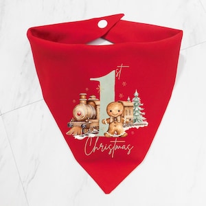 May include: Red Christmas bib with a gingerbread man and train design. The bib has the text "1st Christmas" on it.