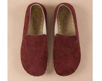May include: A pair of burgundy suede slip-on shoes with a white sole and the text "ATLANTIS" on the inside of each shoe.