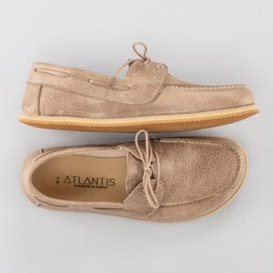 Pu&ograve; includere: Due paia di scarpe da barca beige con lacci, caratterizzate da un aspetto in pelle strutturata e cuciture bianche. Le scarpe hanno una suola marrone chiaro e il marchio "ATLANTIS" &egrave; visibile sulla soletta. Fatto a mano in Turchia.