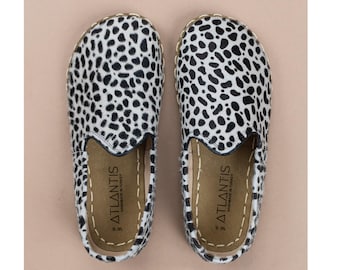 Può includere: Un paio di scarpe slip-on con motivo animalier bianco e nero. Le suole interne sono color cuoio e riportano la scritta ATLANTIS HANDMADE IN TURKEY e W8. Le scarpe presentano cuciture chiare visibili lungo i bordi.