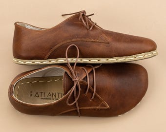 May include: A pair of brown leather lace-up shoes with a rounded toe and visible light-colored stitching along the sole. The interior of the shoe features the text ATLANTIS HANDMADE IN TURKEY and the size W 8 printed on the light-colored insole.