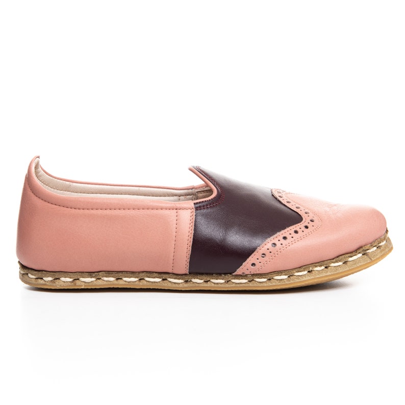 May include: A pair of pink and burgundy leather slip-on shoes with a decorative stitch pattern and a brown jute sole.