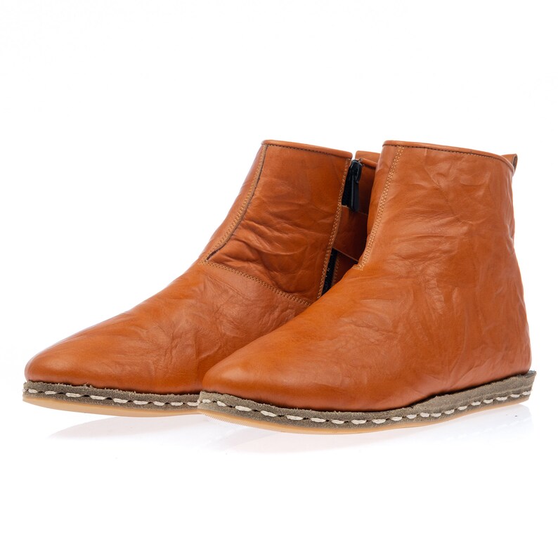 May include: A pair of brown leather ankle boots with a zipper on the side. The boots have a stitched seam around the sole and a white stitching detail.