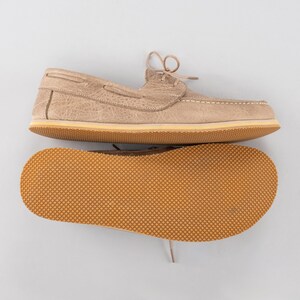 Pu&ograve; includere: Scarpe da barca beige con cuciture e lacci bianchi. La suola &egrave; marrone chiaro con un motivo strutturato. La tomaia della scarpa ha un aspetto strutturato. Le scarpe sono esposte su sfondo bianco.