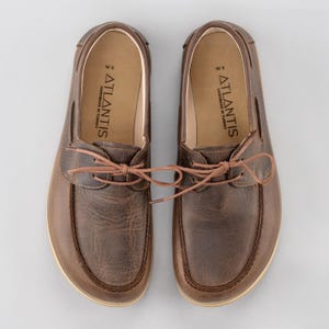 Könnte beinhalten: Ein Paar braune Leder-Bootschuhe mit hellen Sohlen. Die Schuhe haben Schnürsenkel und der Markenname "ATLANTIS" ist auf der Innensohle aufgedruckt. Handgefertigt in der Türkei.