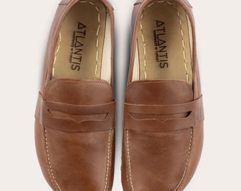 May include: A pair of brown leather loafers with a driving moccasin style. The loafers have a white stitch detail around the edge and a leather strap across the top. The inside of the loafers is lined with a cream-colored fabric and has the text "ATLANTIS HANDMADE IN TURKEY" printed on the insole.