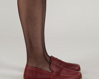 May include: A pair of burgundy leather loafers with a stitched detail on the vamp. The loafers have a rounded toe and a low heel.