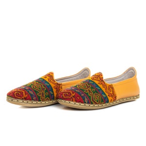 May include: A pair of yellow leather slip-on shoes with a colorful geometric pattern on the front. The shoes have a flat sole and a pointed toe.