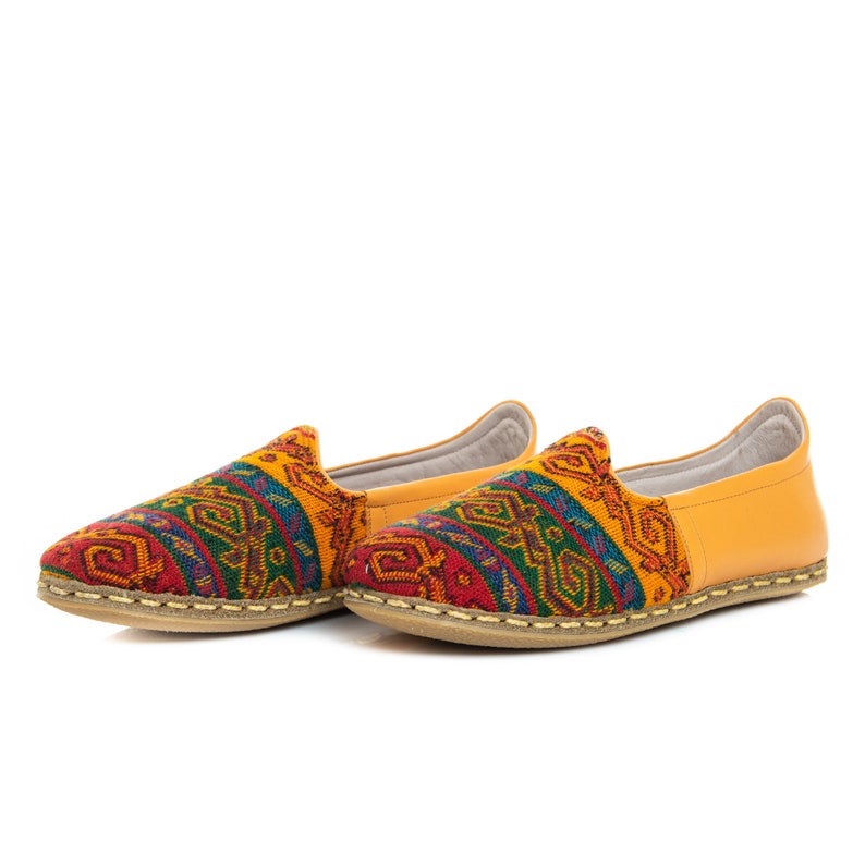 May include: A pair of yellow leather slip-on shoes with a colorful geometric pattern on the front. The shoes have a flat sole and a pointed toe.