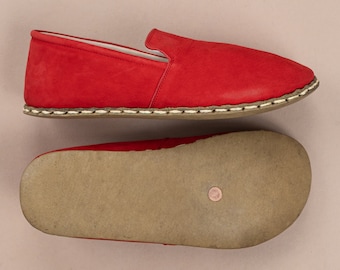 May include: A pair of red leather slip-on shoes with a white stitching detail around the edge. The shoes are shown from the top and bottom.