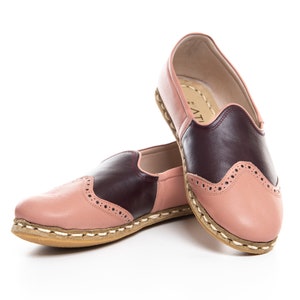 May include: A pair of pink and burgundy leather slip-on shoes with a decorative stitch pattern. The shoes have a brown sole and a white stitching detail around the edge.