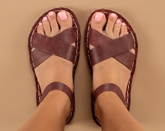 May include: A pair of brown leather sandals with criss-cross straps. The sandals have a simple design and are perfect for summer.