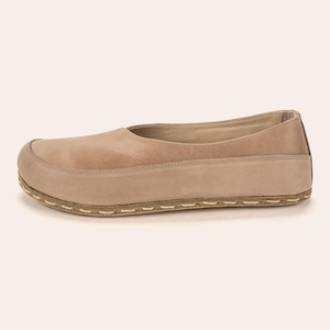 May include: A single beige leather shoe with a rounded toe and a low profile. The shoe features a stitched sole and a smooth upper, with a darker shade of beige at the heel. The shoe is designed for comfort and casual wear.