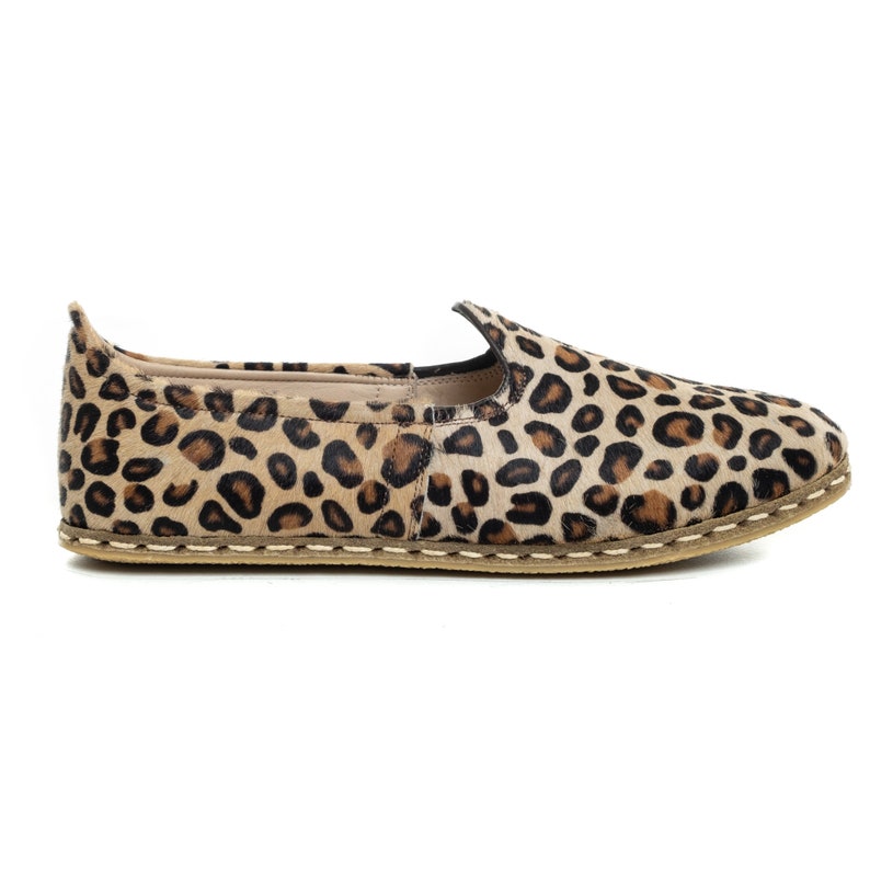May include: Leopard print slip-on shoes with a brown leather upper and a beige sole.