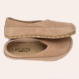 May include: Two pairs of tan-colored leather slip-on shoes. The shoes have a rounded toe and a stitched sole. The brand name "ATLANTIS" is visible on the insole of one shoe. The shoes are size W8.