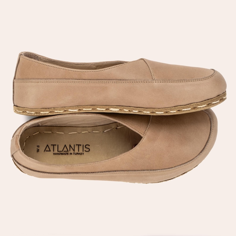 May include: Two pairs of tan-colored leather slip-on shoes. The shoes have a rounded toe and a stitched sole. The brand name "ATLANTIS" is visible on the insole of one shoe. The shoes are size W8.