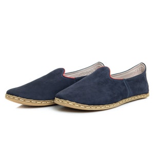 May include: A pair of dark blue suede slippers with a red trim and a light brown sole.