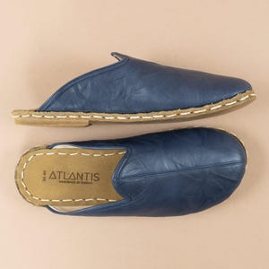 May include: Two pairs of blue leather slip-on shoes. The shoes have a rounded toe, a tan sole, and white stitching around the edges. The insole of one shoe has the word "ATLANTIS" printed on it. The shoes are handmade in Turkey.