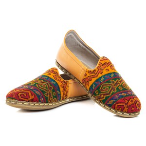 May include: A pair of yellow leather slippers with colorful geometric patterns. The slippers have a pointed toe and a flat sole.