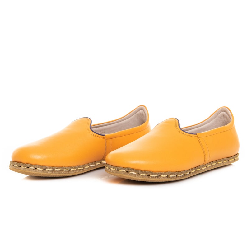 May include: A pair of yellow leather slip-on shoes with a brown stitched sole.