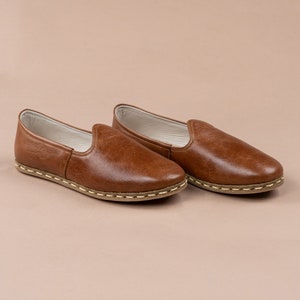 May include: A pair of brown leather slip-on shoes with a white stitch detail around the sole.