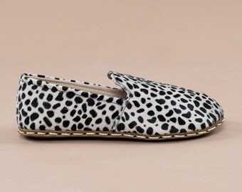 Può includere: Un paio di scarpe da barca in pelle bianca e nera con stampa animalier e un bordo dorato intorno alla suola.