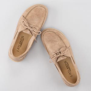 Pu&ograve; includere: Un paio di scarpe da barca beige con lacci, su sfondo grigio chiaro. Le scarpe hanno un aspetto in pelle strutturata. Il marchio "ATLANTIS" &egrave; visibile sulla soletta interna. Fatte a mano in Turchia.