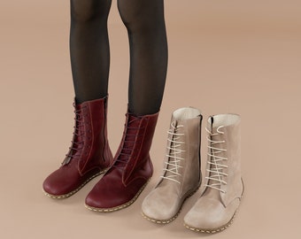 May include: Two pairs of ankle boots. One pair is a deep burgundy color with laces and a side zipper. The other pair is a light tan color with laces. Both pairs have a minimalist design and are made of leather.