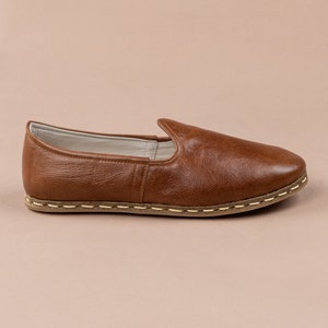 May include: A pair of brown leather slip-on shoes with a stitched edge and a light brown sole.
