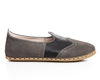 May include: Gray suede slip-on shoes with a black leather panel and a white stitching detail around the sole.