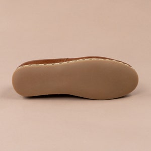 May include: The underside of a brown leather loafer with white stitching around the edge.
