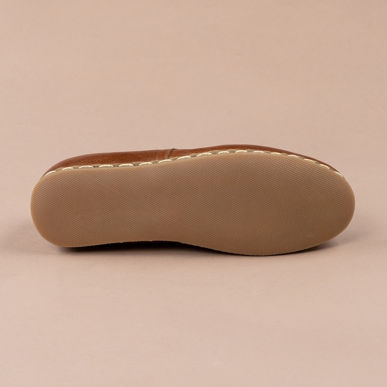May include: The underside of a brown leather loafer with white stitching around the edge.