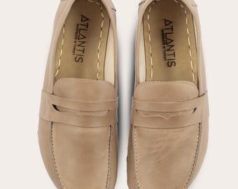 May include: A pair of light brown leather loafers with a stitched detail around the edge. The loafers have a single strap across the top with a small buckle. The inside of the loafers is lined with a cream-colored fabric and has the text "ATLANTIS HANDMADE IN TURKEY" printed on the insole.