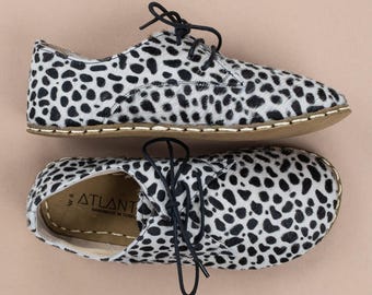 Può includere: Un paio di scarpe stringate con un motivo a macchie bianche e nere. Le scarpe hanno lacci neri, una suola color cuoio con cuciture a vista e la soletta interna riporta la scritta ATLANT e HANDMADE IN TURKEY.