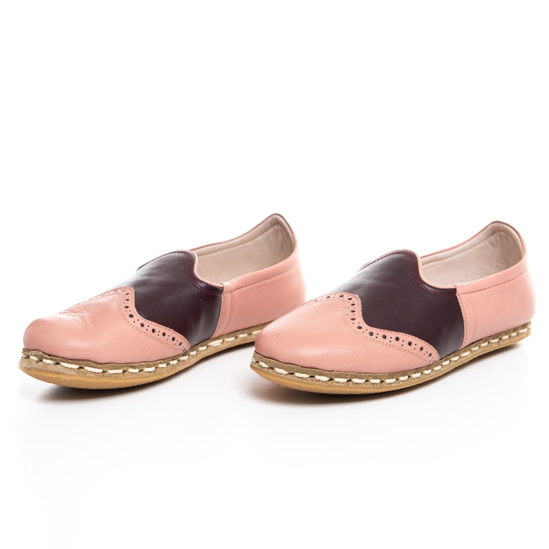 May include: A pair of pink and burgundy leather slip-on shoes with a decorative stitch pattern. The shoes have a white rubber sole.