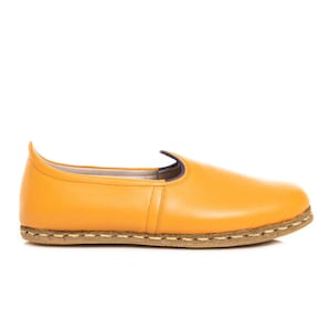 May include: A pair of yellow leather slip-on shoes with a brown stitched sole.