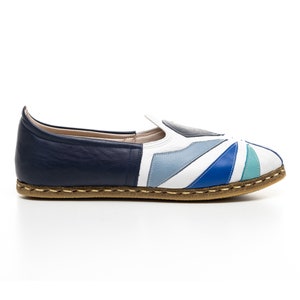 May include: A pair of white leather slip-on shoes with a blue, teal, and gray geometric pattern. The shoes have a brown leather sole.